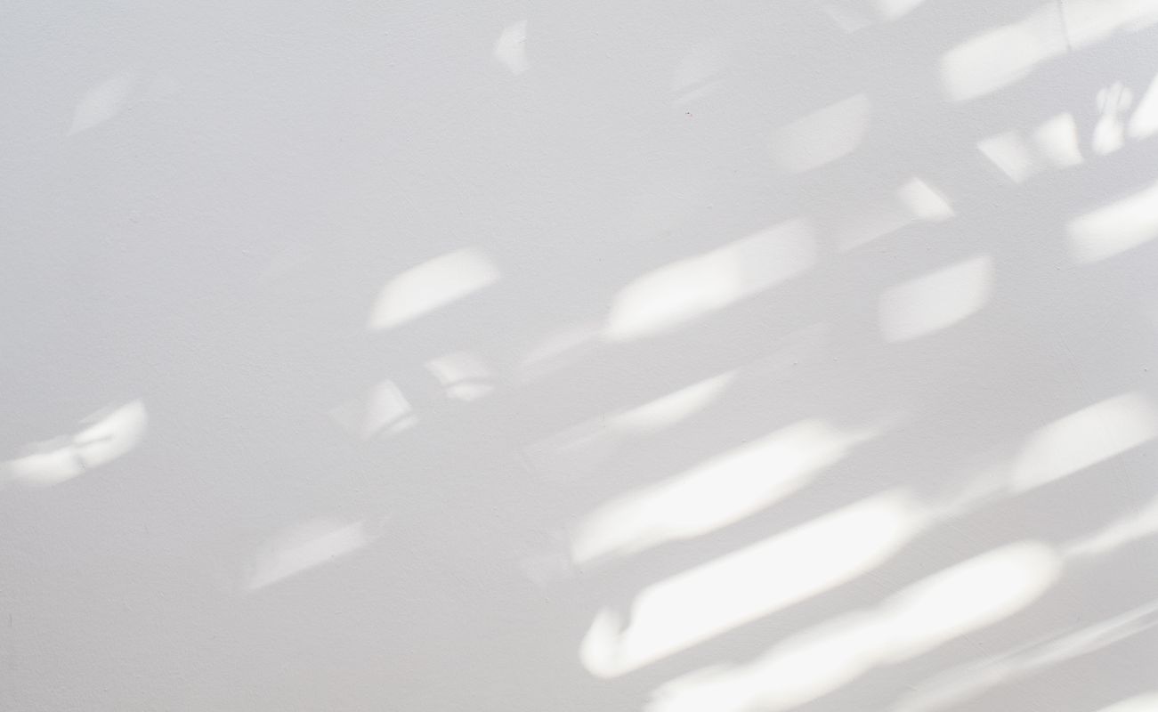 Schattenspiele auf einer weißen Wand, erzeugt durch Licht, das durch Jalousien fällt.