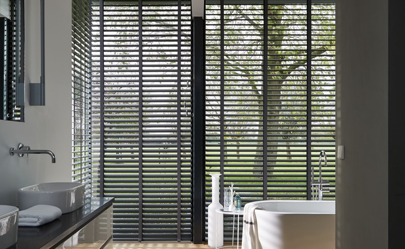 Modern Badezimmer mit freistehender Badewanne, großen Fenstern und Blick auf einen Garten. Helle Farben und minimalistisches Design.